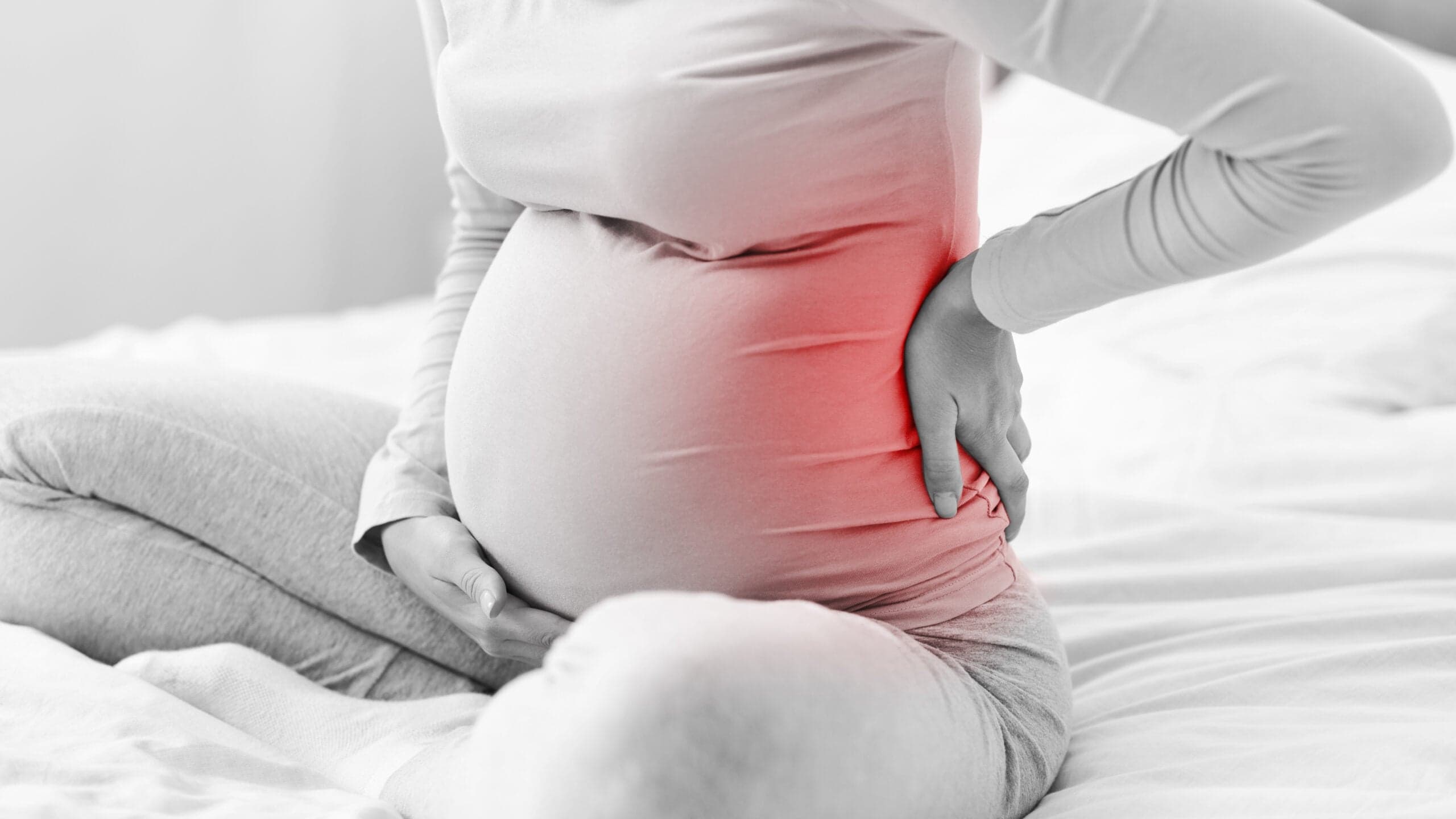 Pregnant woman supporting her lower back — pregnancy-related back, hip, shoulder, and wrist pain often responds to a whole-body physical therapy approach